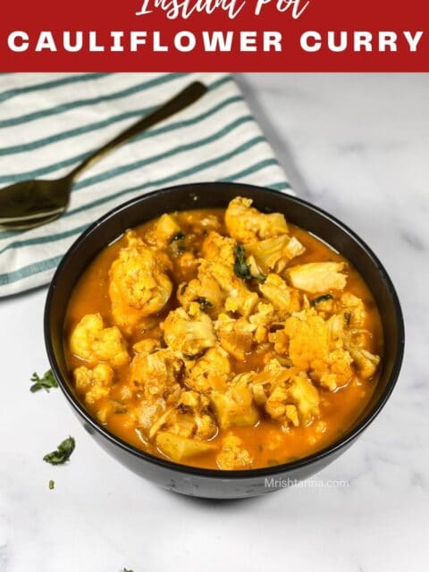 A bowl of cauliflower coconut curry is on the white surface with a spoon.