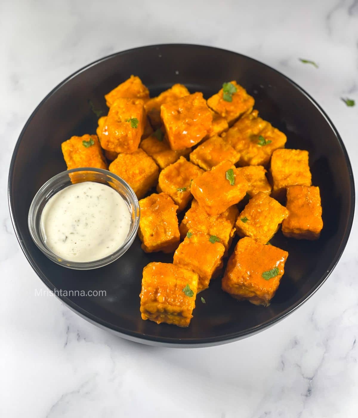 A plate is with air fried buffalo tofu and vegan ranch dip.