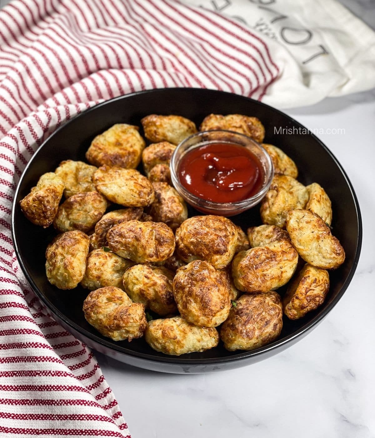 A plate of homemade tater tots are on the table with ketchup. 