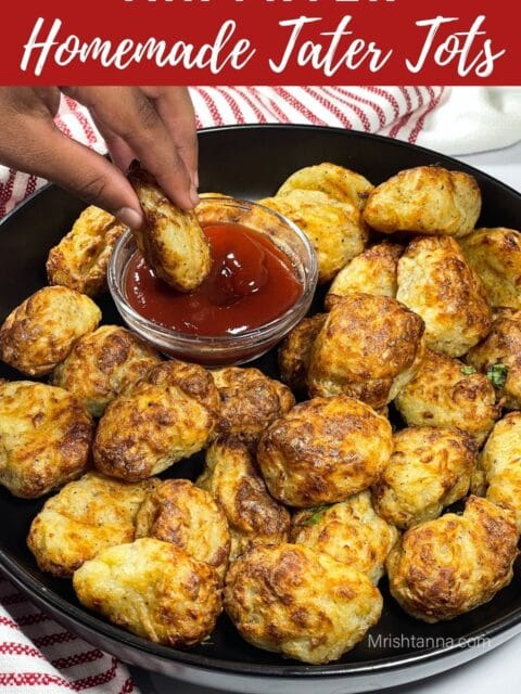 A little hand is dipping tater tots into ketchup.