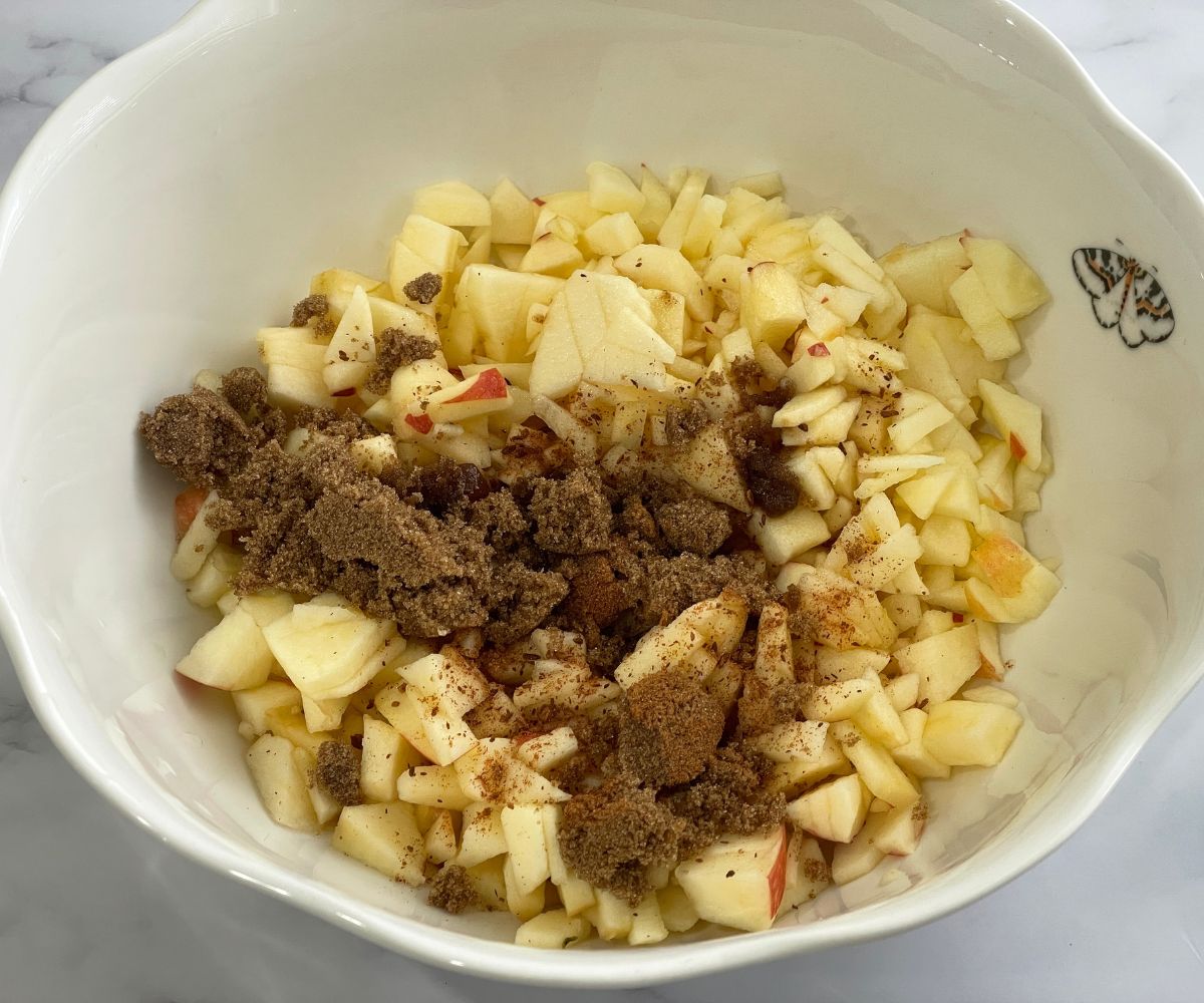 A large bowl is with diced apples, cinnamon and brown sugar.