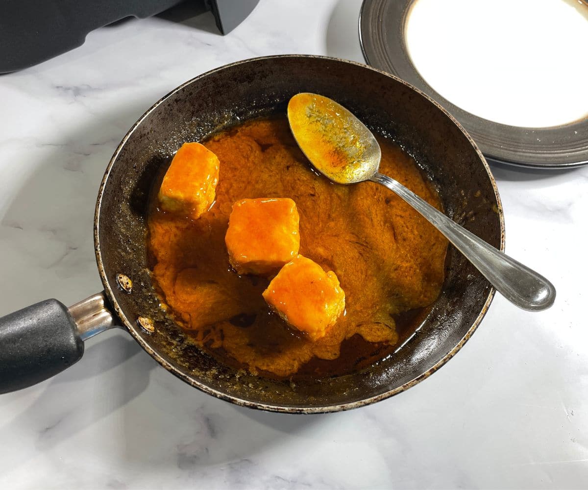 A pan is with buffalo sauce coated tofu bites.