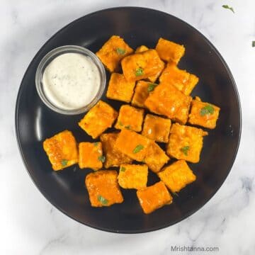 A plate of buffalo tofu is on the table with dipping sauce.