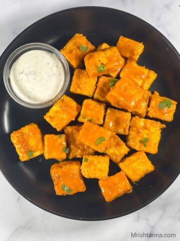 A plate of buffalo tofu is on the table with dipping sauce.