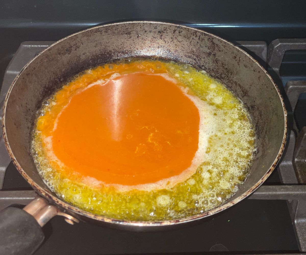 A heated pan is with buffalo sauce and melted vegan butter.