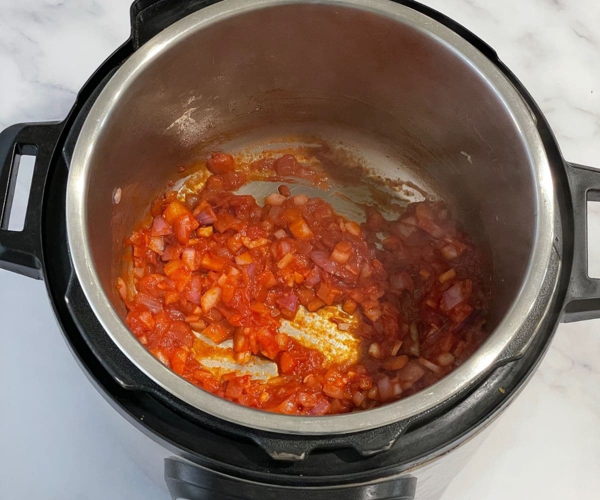 A pot is with onions and tomato paste on saute mode.