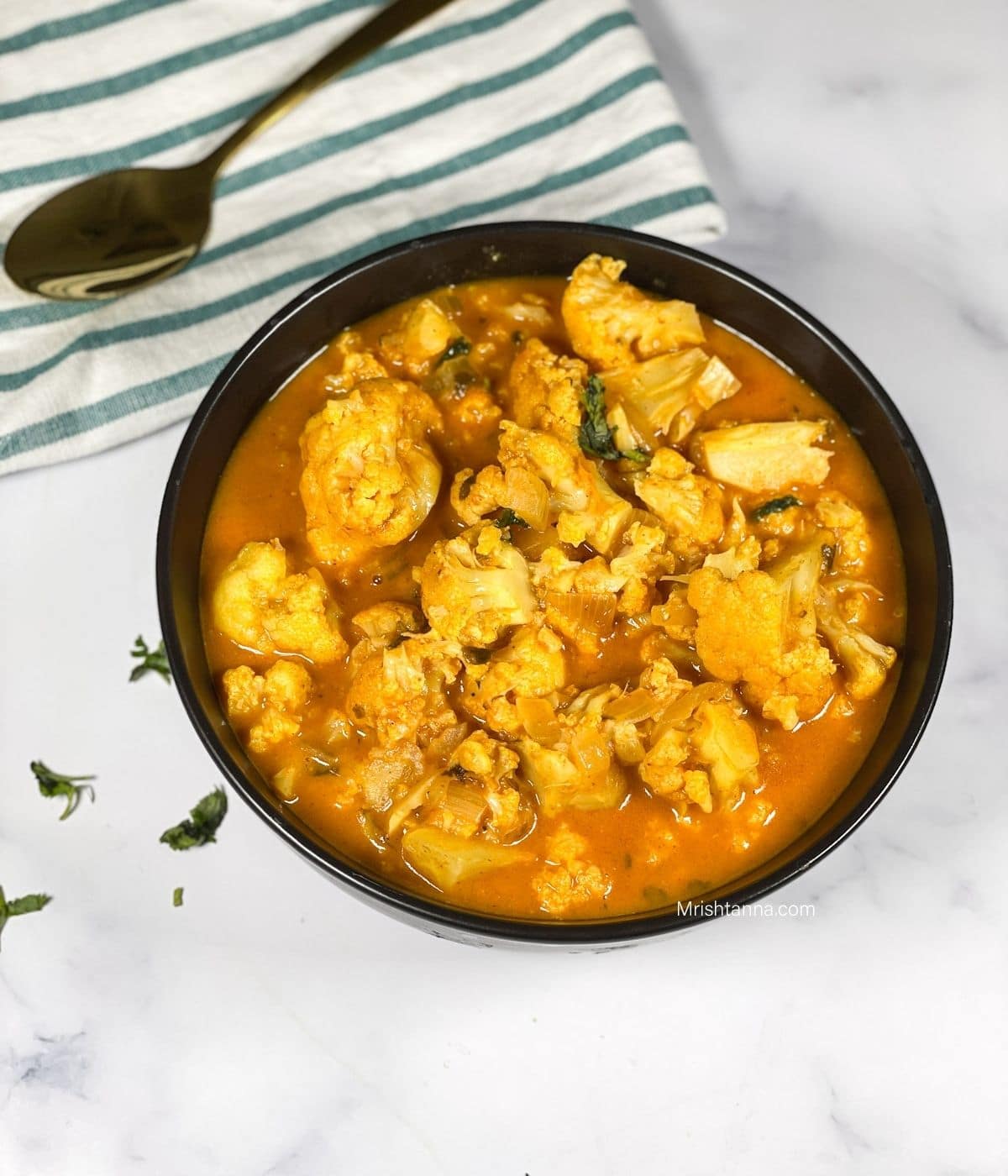 A black bowl of cauliflower curry is on the white marble counter top.