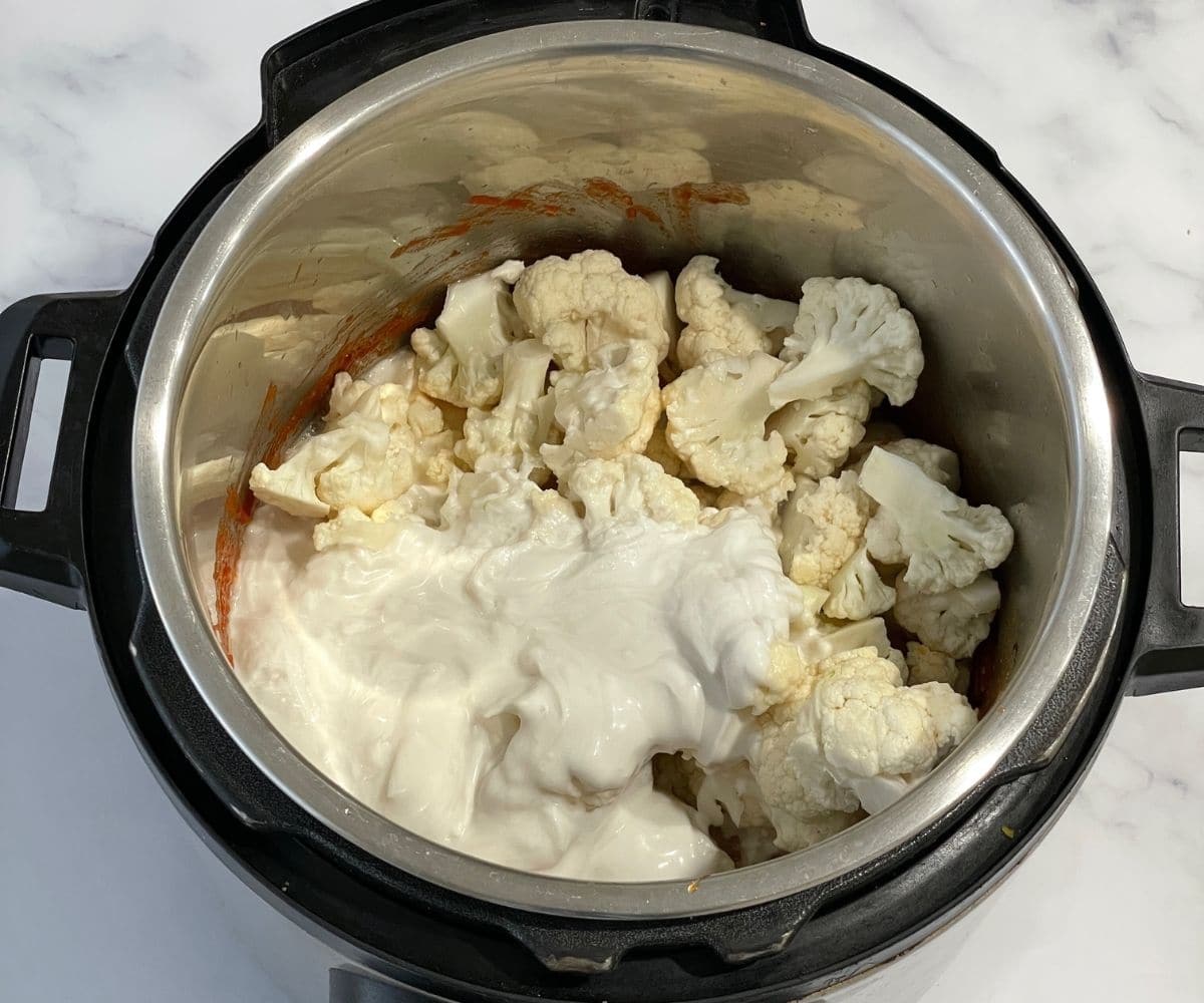 An instant pot is with cauliflower florets and coconut milk for curry.