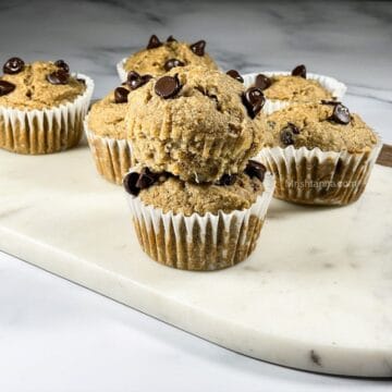Two stacked vegan banana muffins are topped with chocolate chips.