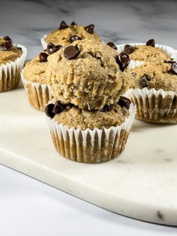 Two stacked vegan banana muffins are topped with chocolate chips.
