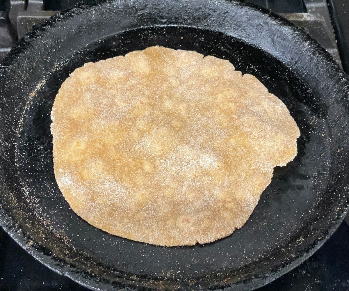 A cast iron skillet is with gluten free chapati over medium flame.