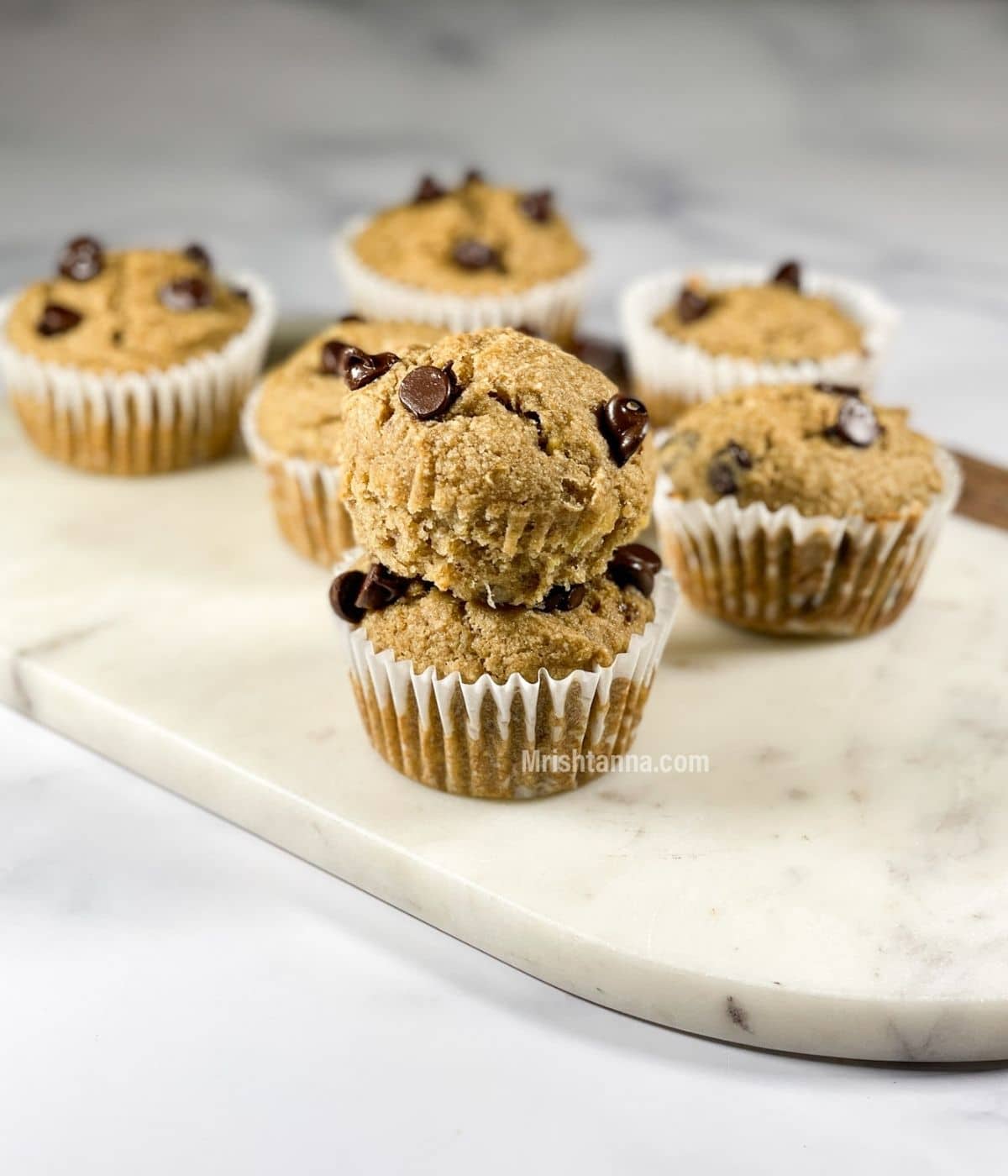 Two gluten free banana muffins are stacked on the white tray.