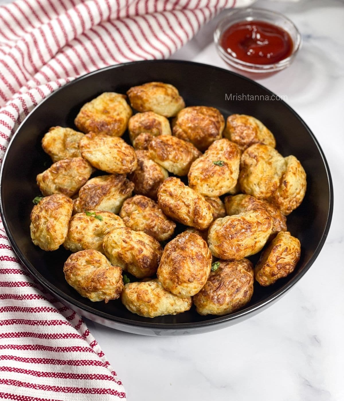 A plate of homemade tater tots are on the table with ketchup on side.