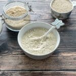 A bowl of homemade quinoa flour is on the table along with dry quinoa on the side.