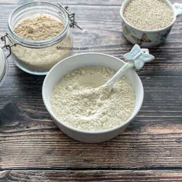 A bowl of homemade quinoa flour is on the table along with dry quinoa on the side.