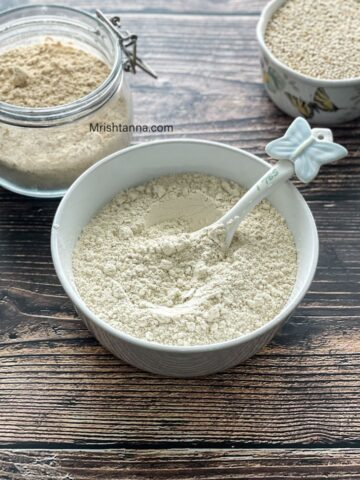 A bowl of homemade quinoa flour is on the table along with dry quinoa on the side.