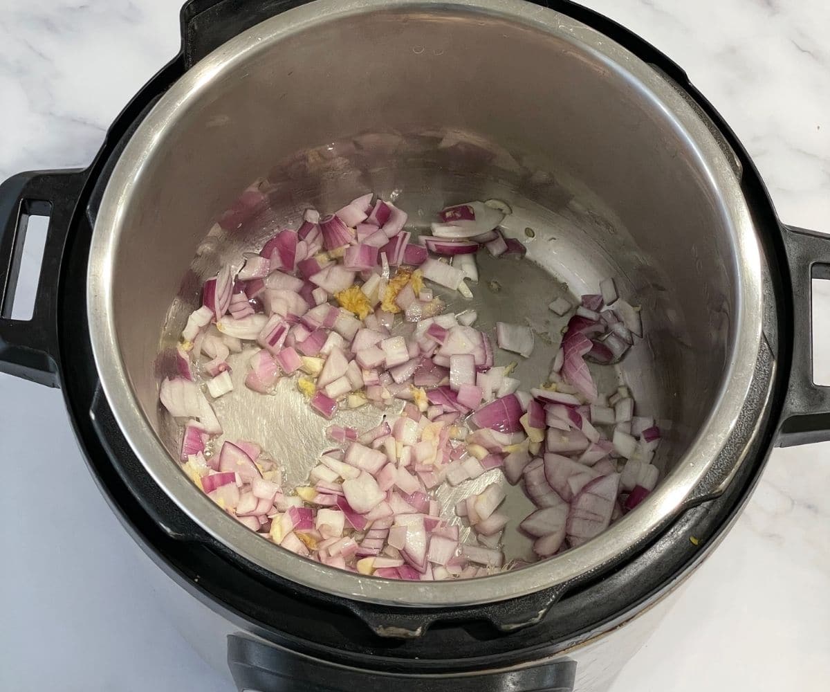 An instant pot is with onions, ginger and garlic on saute mode.