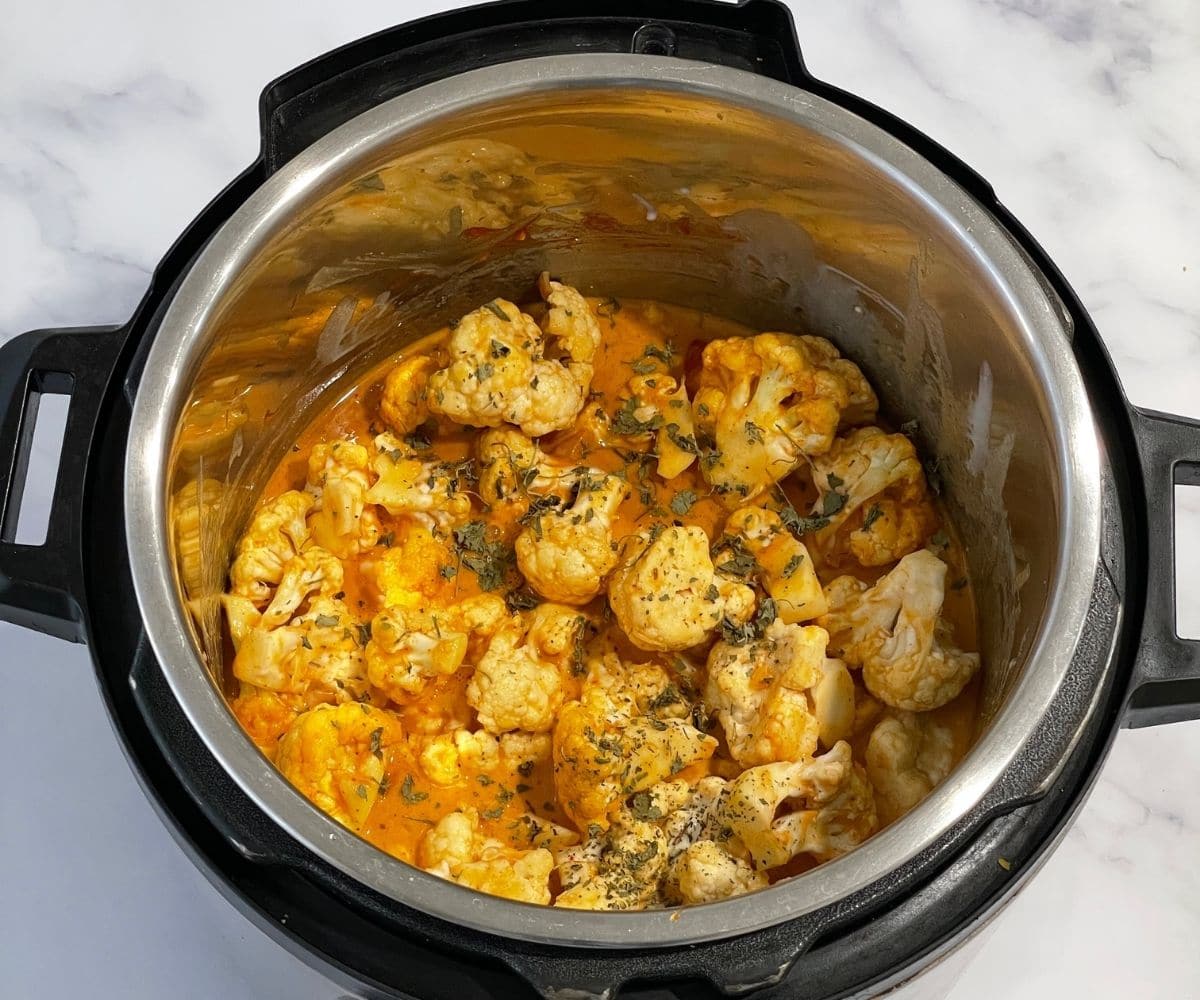 An instant pot is filled with cauliflower and spices for curry.
