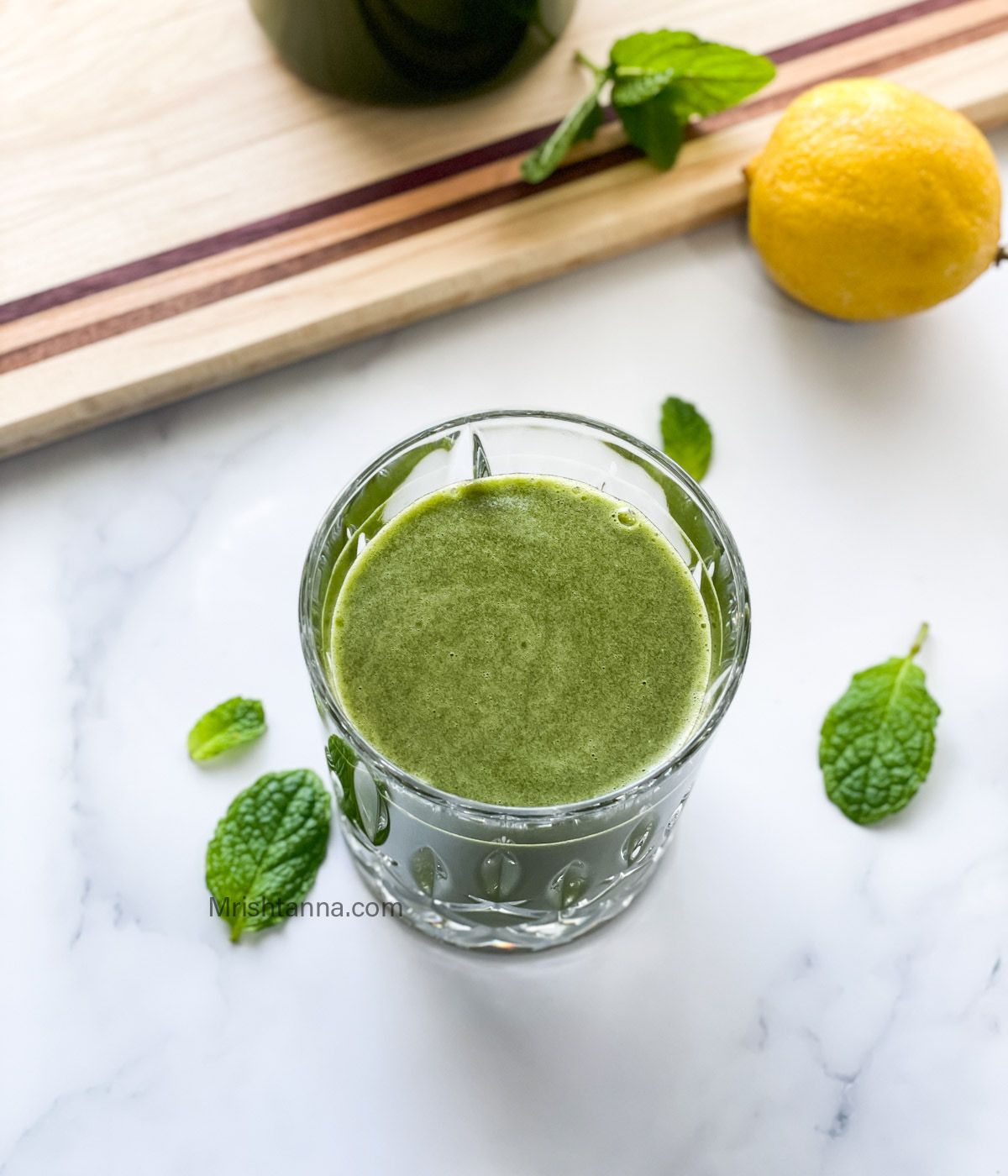 A glass of lemon mint juice is on the white surface.