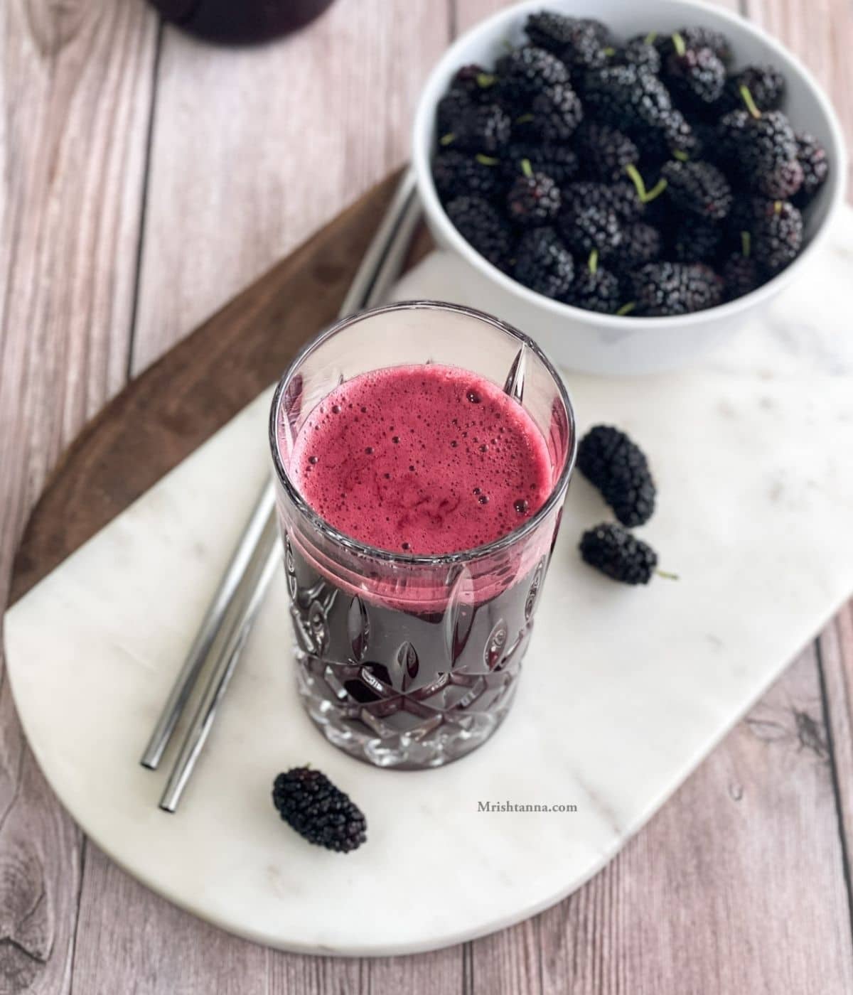 A glass of mulberry juice is on the table with steel straws.