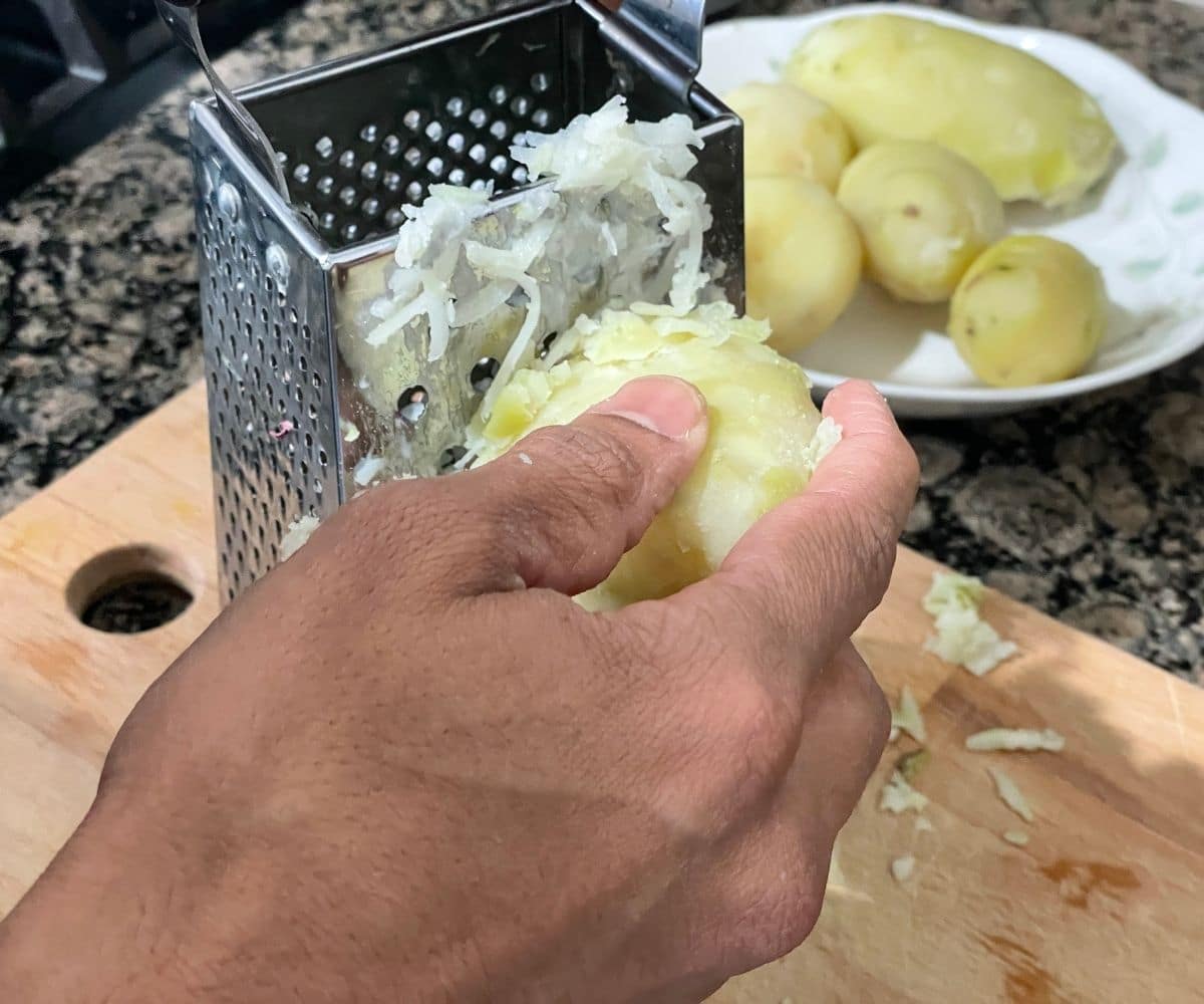 A man is grating potatoes using grater.