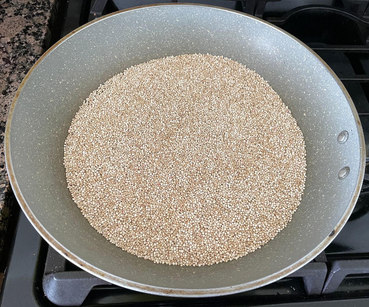 A pan is with dry quinoa over the stove top.