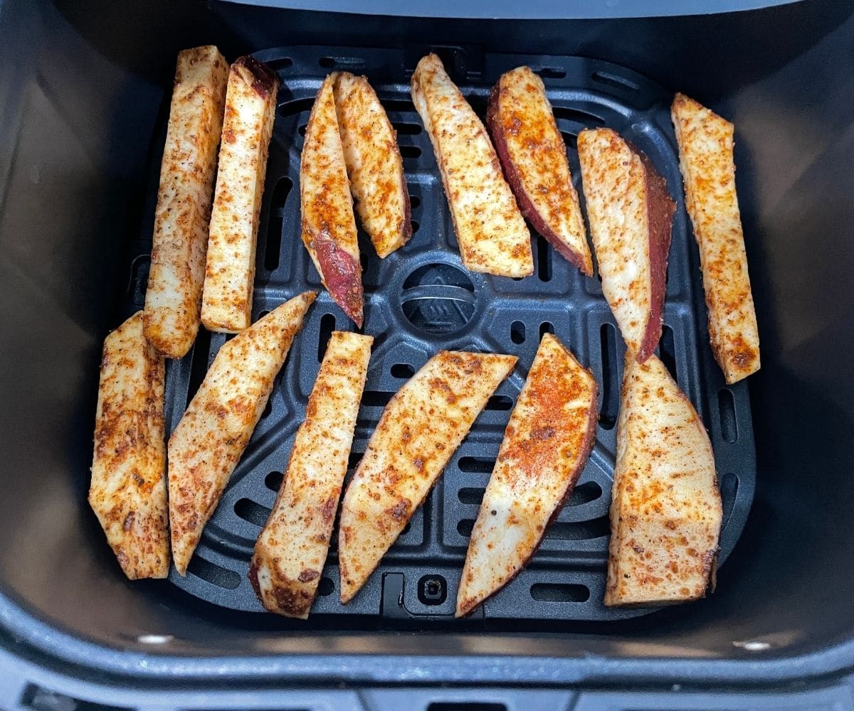 Air fryer basket is with spice coated sweet potatoes.