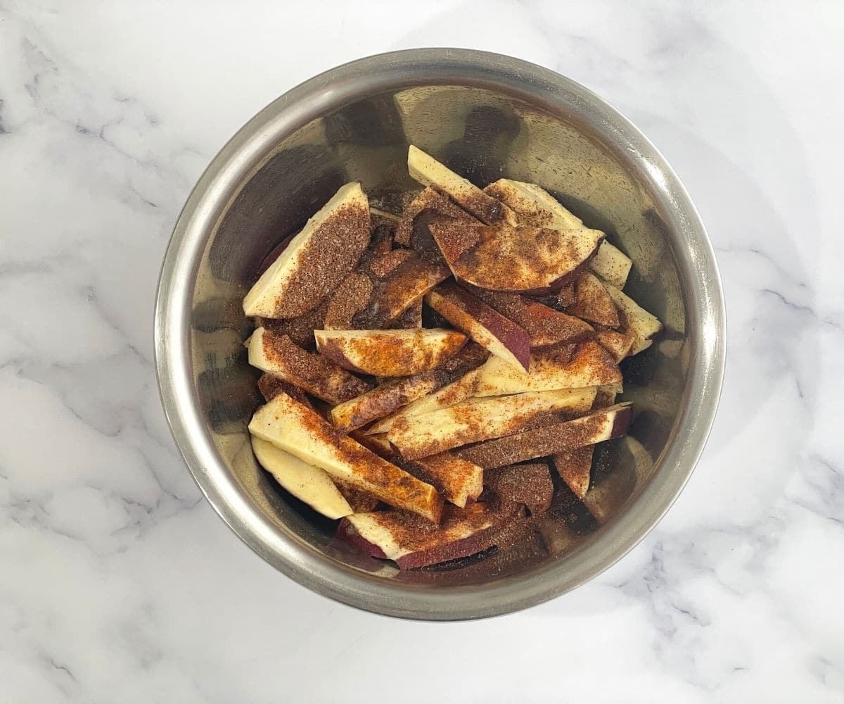 A bowl is with sweet potato wedges and spices.