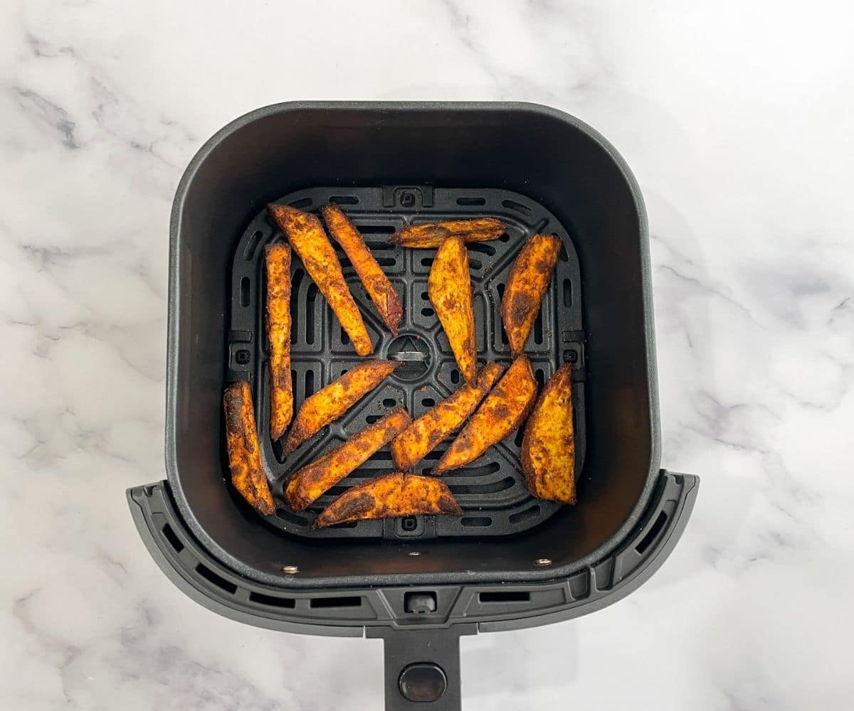 Air fryer basket is with sweet potato wedges.