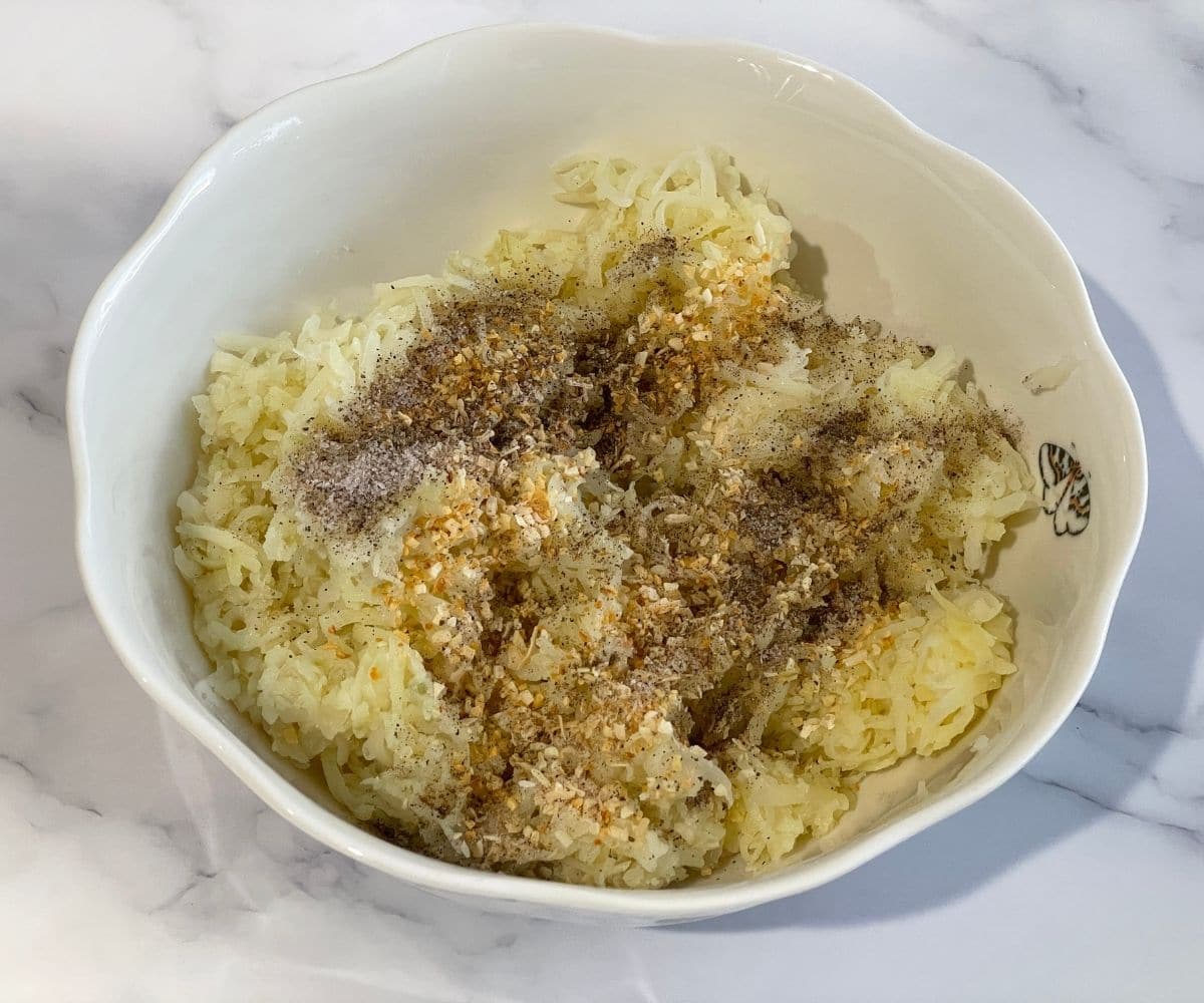 A bowl is with grated potatoes, and spices.