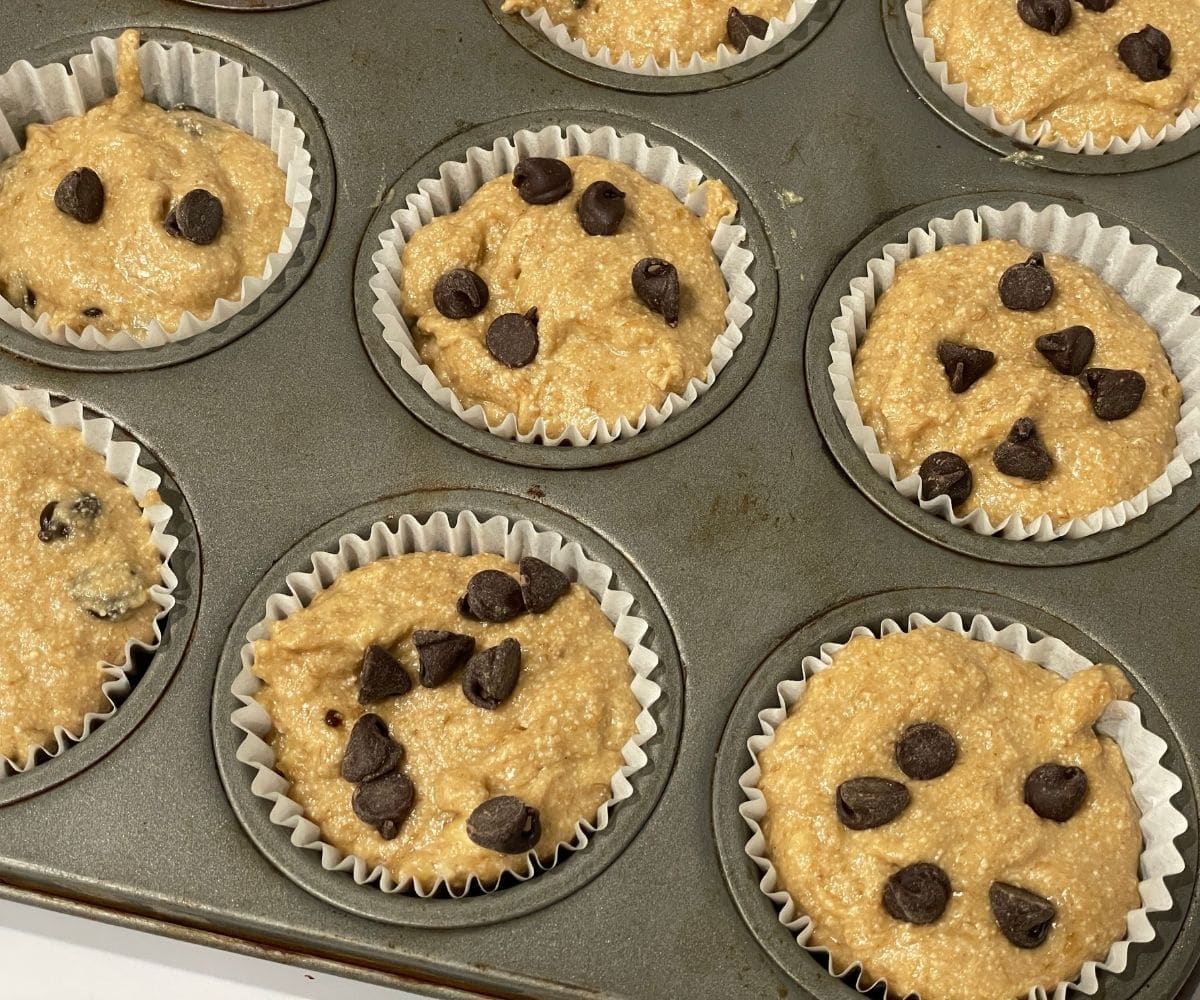 A muffin tray is filled with quinoa flour banana muffins and topped with chocolate chips.