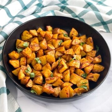 A black ceramic plate is with air fryer potato cubes.