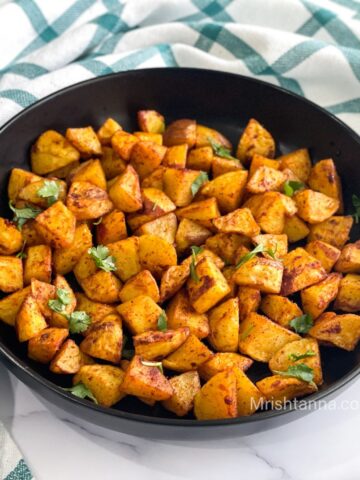 A black ceramic plate is with air fryer potato cubes.