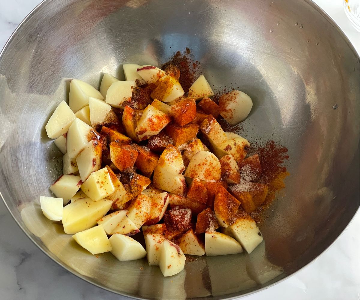 A bowl is with diced potatoes, spices and salt.