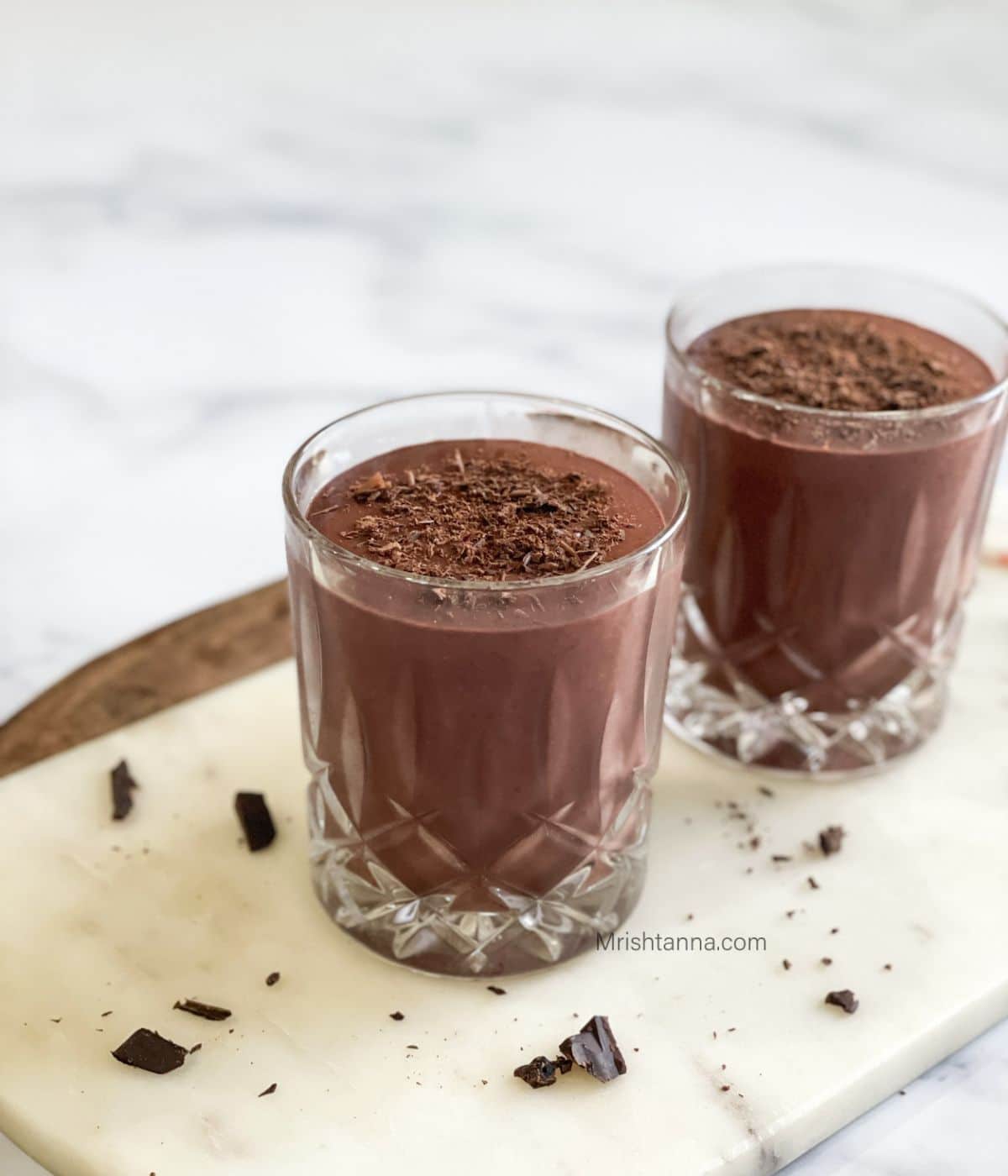 Two glasses are filled with cherry smoothie and placed on  white marble tray.