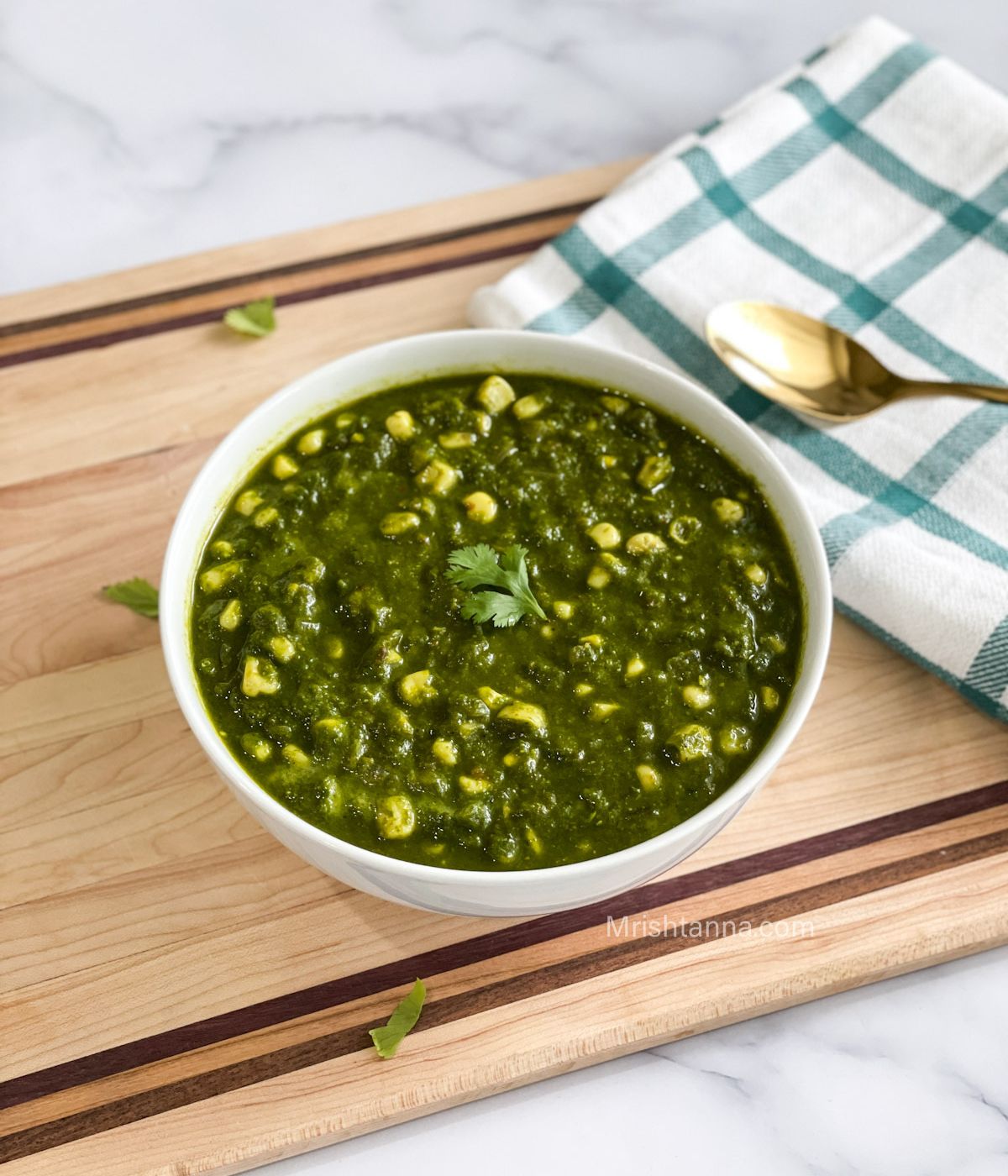 A bowl of corn palak curry is on the wooden board.