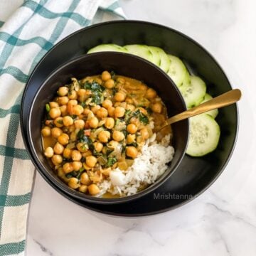 A bowl of chickpea curry with spinach is on the table.