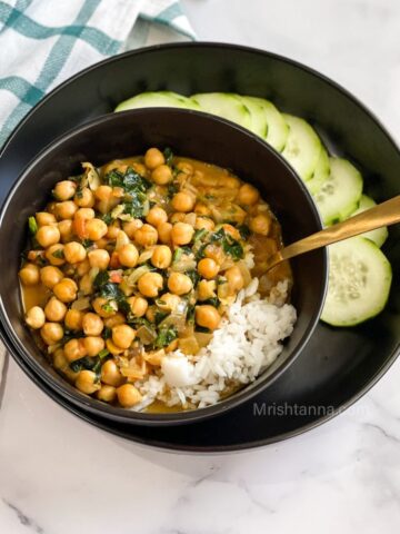A bowl of chickpea curry with spinach is on the table.