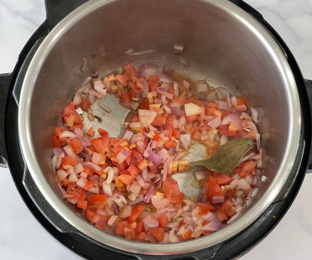 An instant pot is with tomatoes and onions on saute mode.