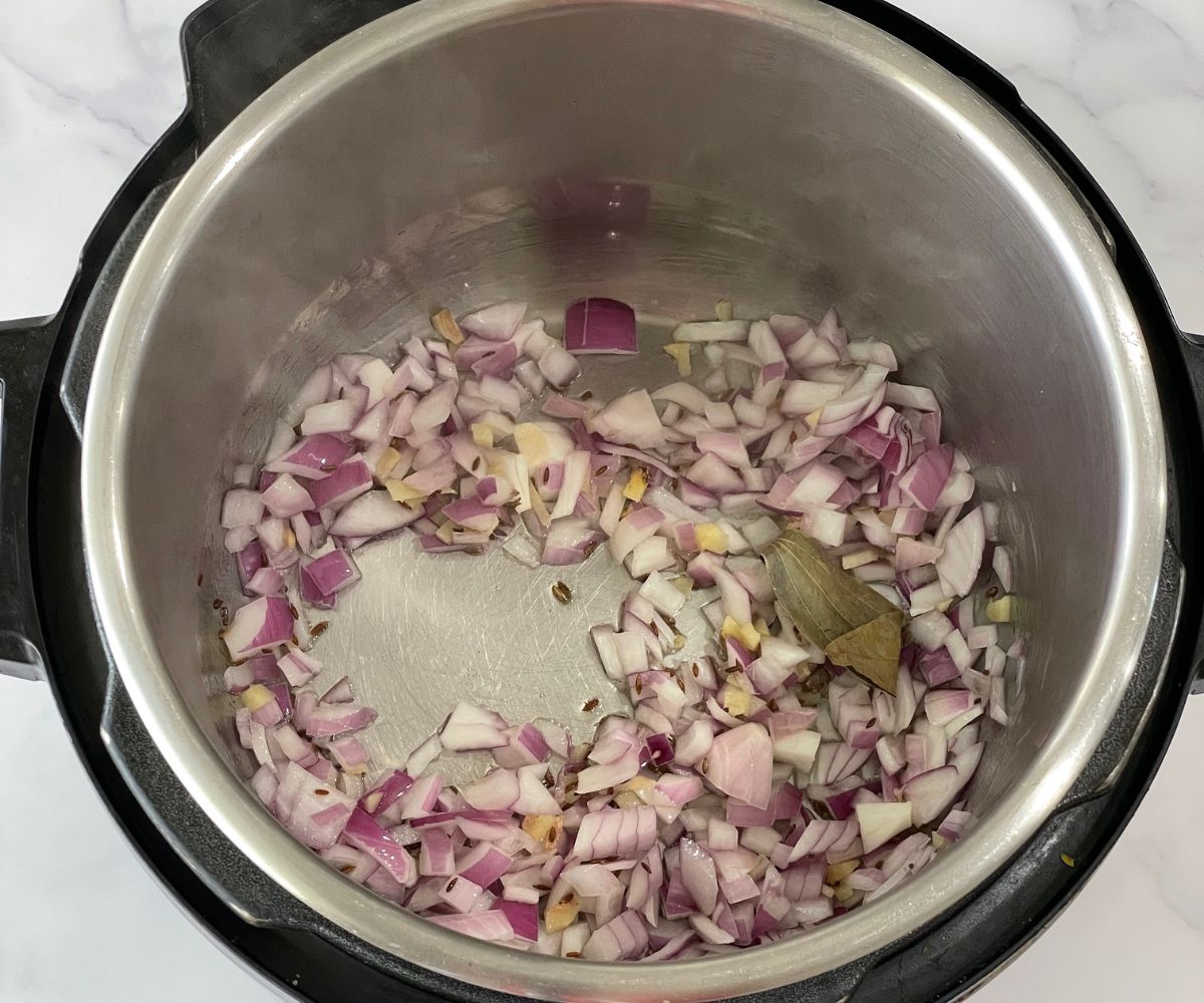 An instant pot is with spices and onions for chickpeas curry.