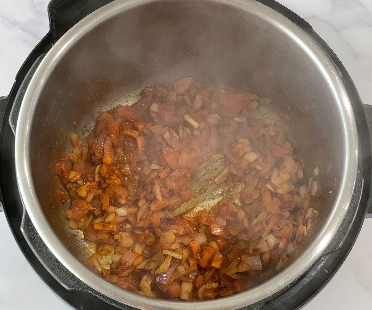 A pot is with spices and tomato mixture on saute mode.