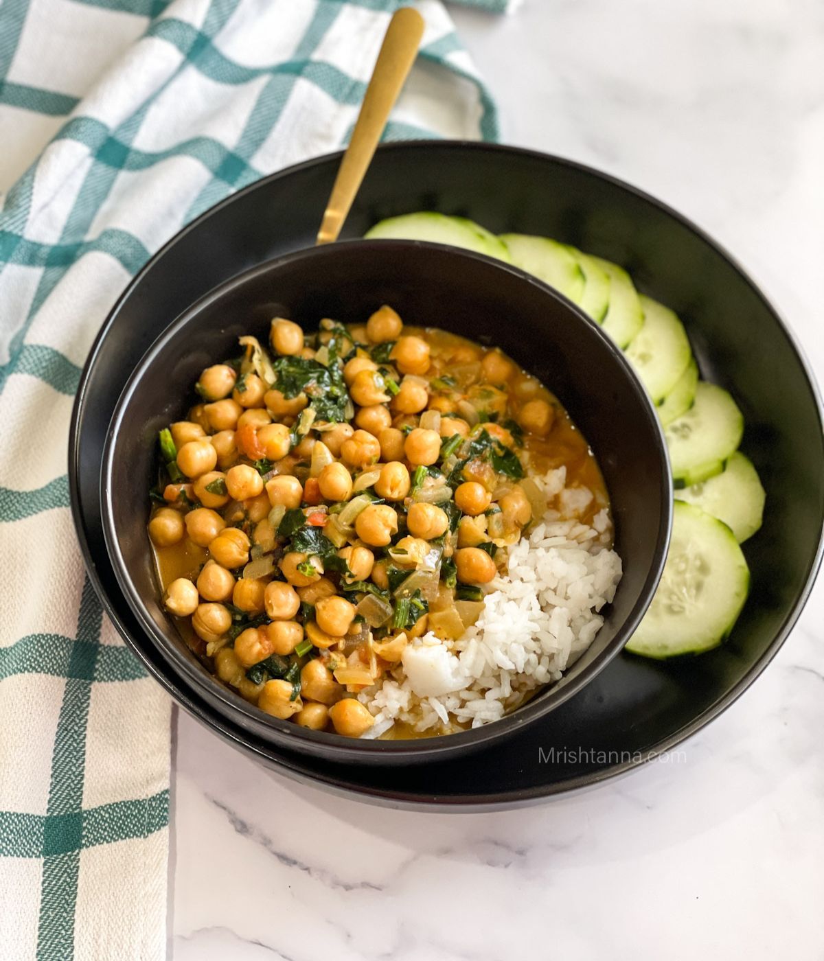 A bowl of instant pot chickpea curry is on the plate with sliced cucumbers.