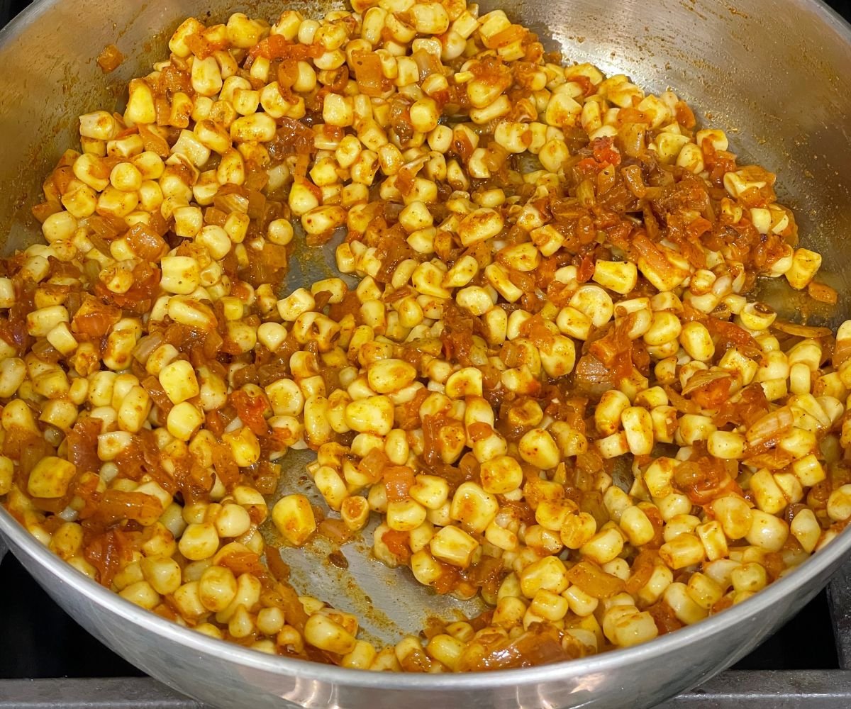 A pot is with corn kernels and spices over the heat for palak corn curry.