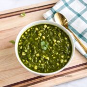 A bowl of spinach corn curry is on the table with a spoon.