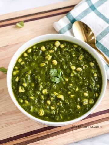 A bowl of spinach corn curry is on the table with a spoon.