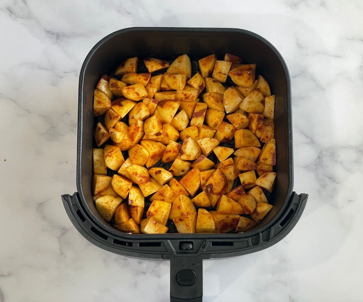 Potato cubes are on air fryer basket.