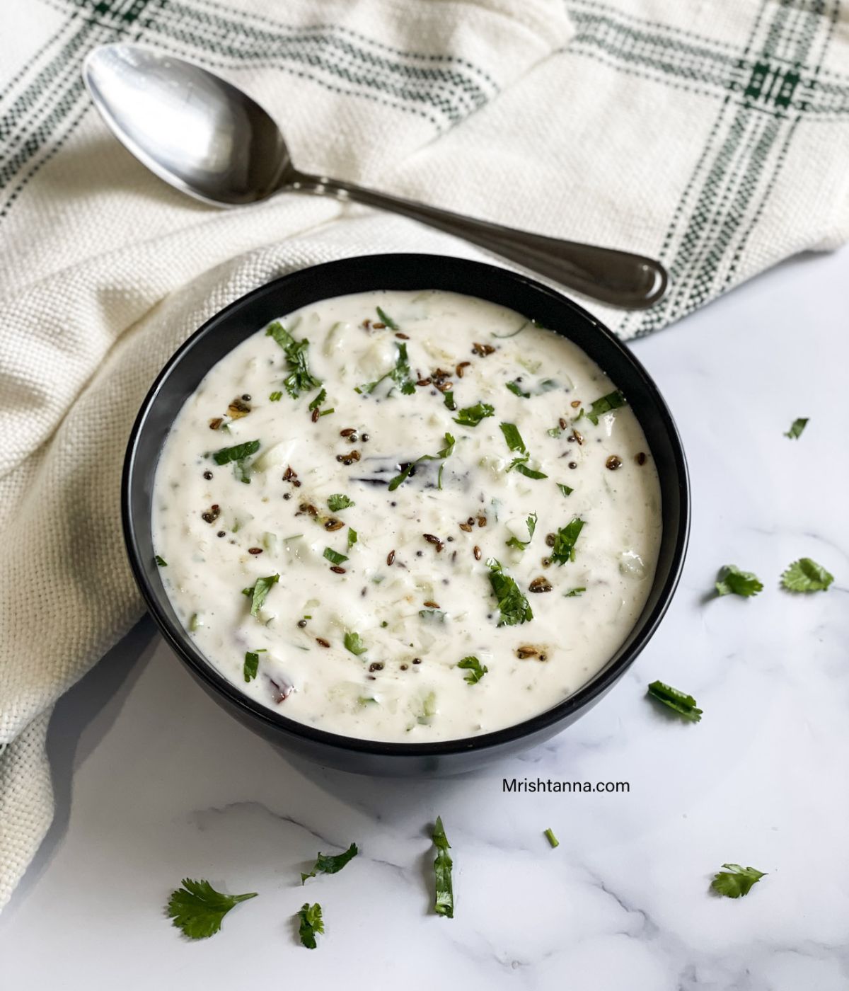 A bowl of vegan raita is on the marble table.