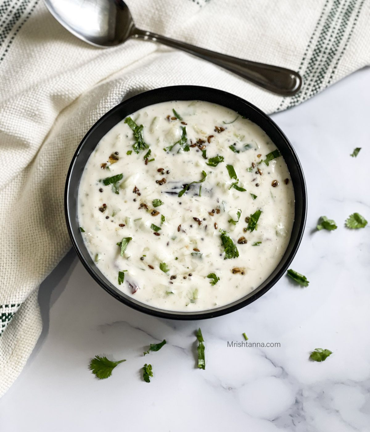 A bowl of vegan raita is placed on the white marble flour.