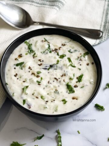 A black color bowl is with vegan raita.