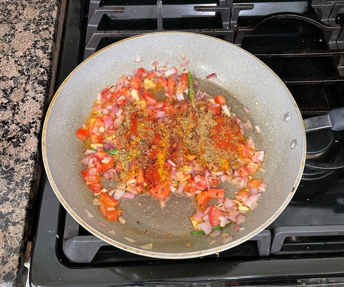 a pan is with tomatoes and spice powders over the heat.